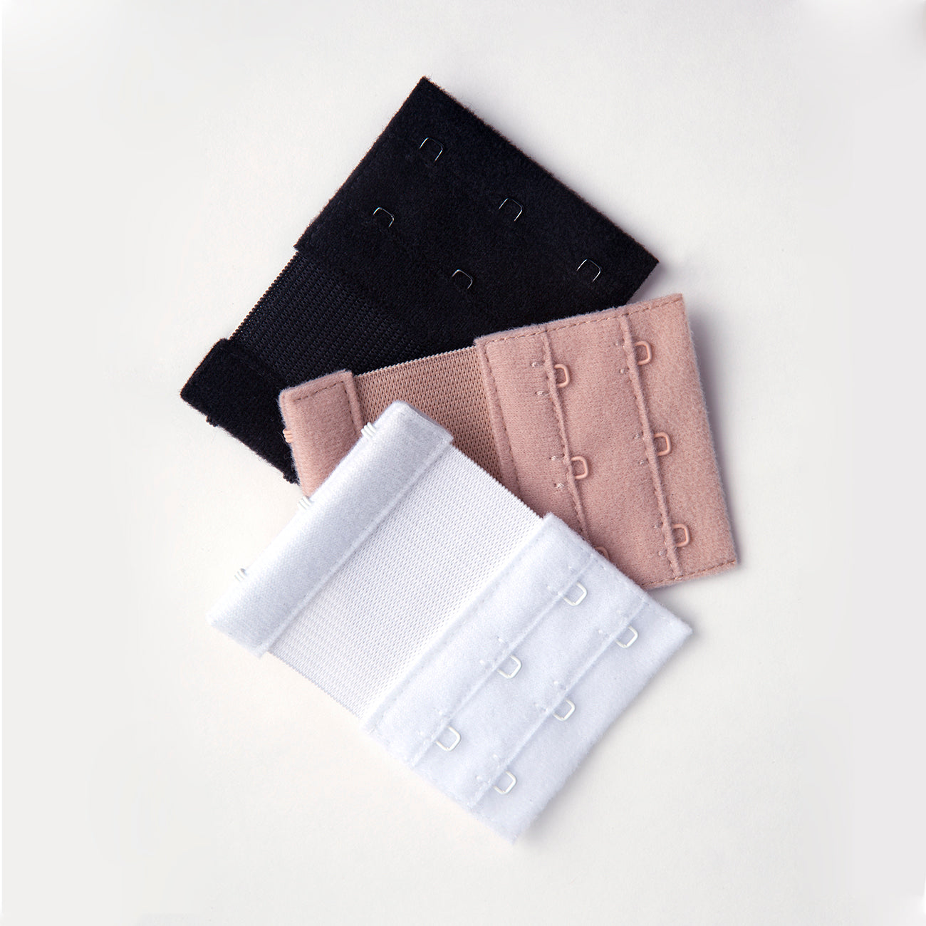 Close up of the 3 hook bra extenders. They are soft nylon in three separate colors with metal hooks. The colors are black, white, and beige.