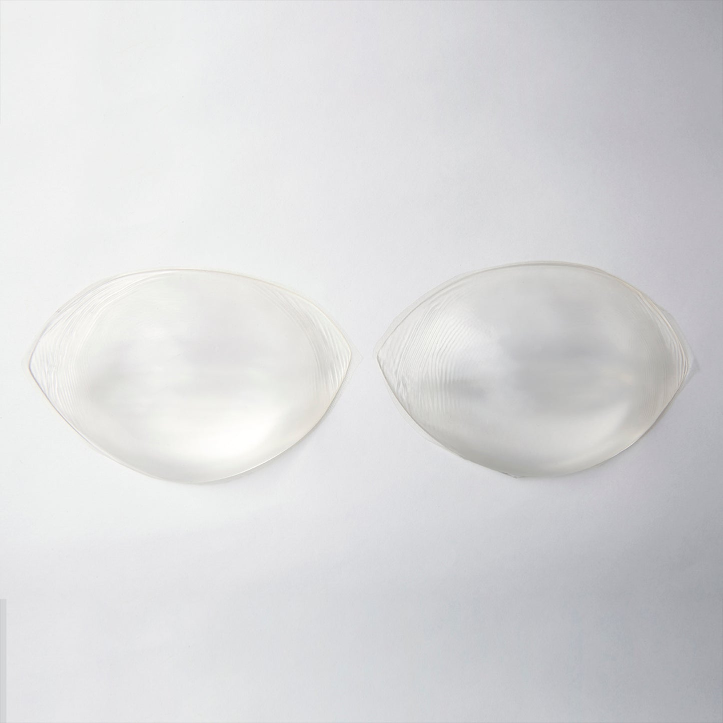 Product image of the silicone push up pads. They are clear and provide lift when inserted into your bra. They are a small oval shape with edges on either side that taper to a point.