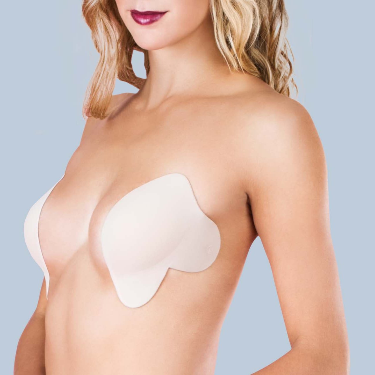 Model wearing the Le Lusion Bra, showing the side where it adheres to the skin. They are two separate cups, leaving plenty of space in the center of the chest for plunging necklines. Bra is light tan in color.