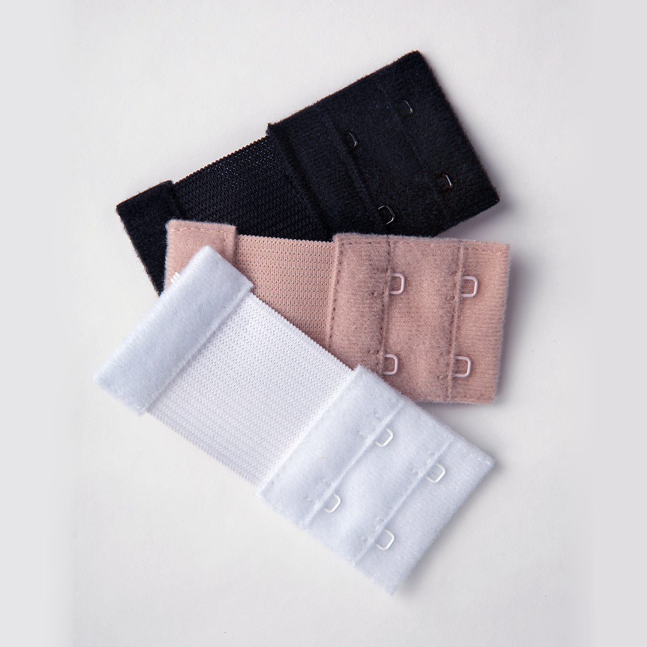 Close up of the 2 hook bra extenders. They are soft nylon in three separate colors with metal hooks. The colors are black, white, and beige.