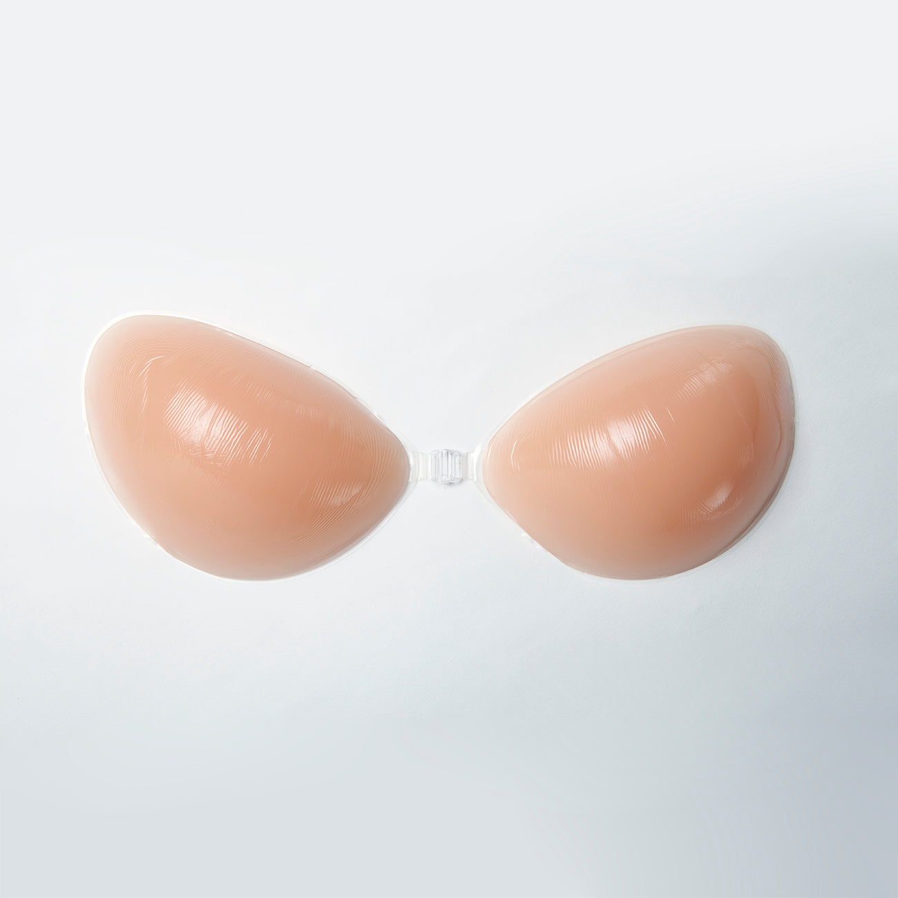 Close up of the nubra on its own. It is facing up, inside of cups facing down. You can see the shaped outside and the clip in the middle. Bra is nude in color.