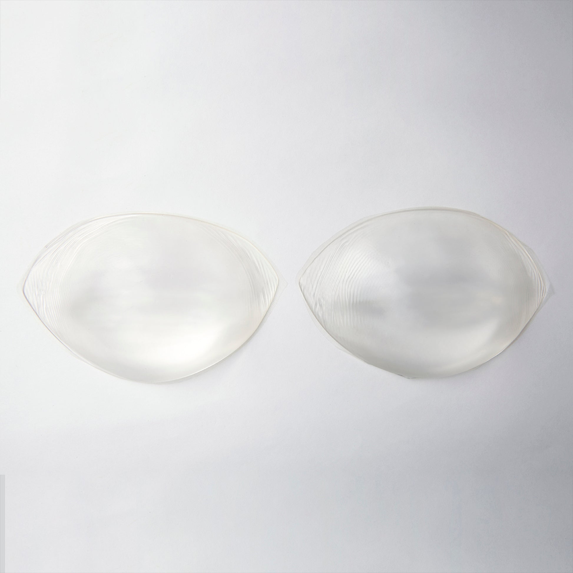 Product image of the silicone push up pads. They are clear and provide lift when inserted into your bra. They are a small oval shape with edges on either side that taper to a point.